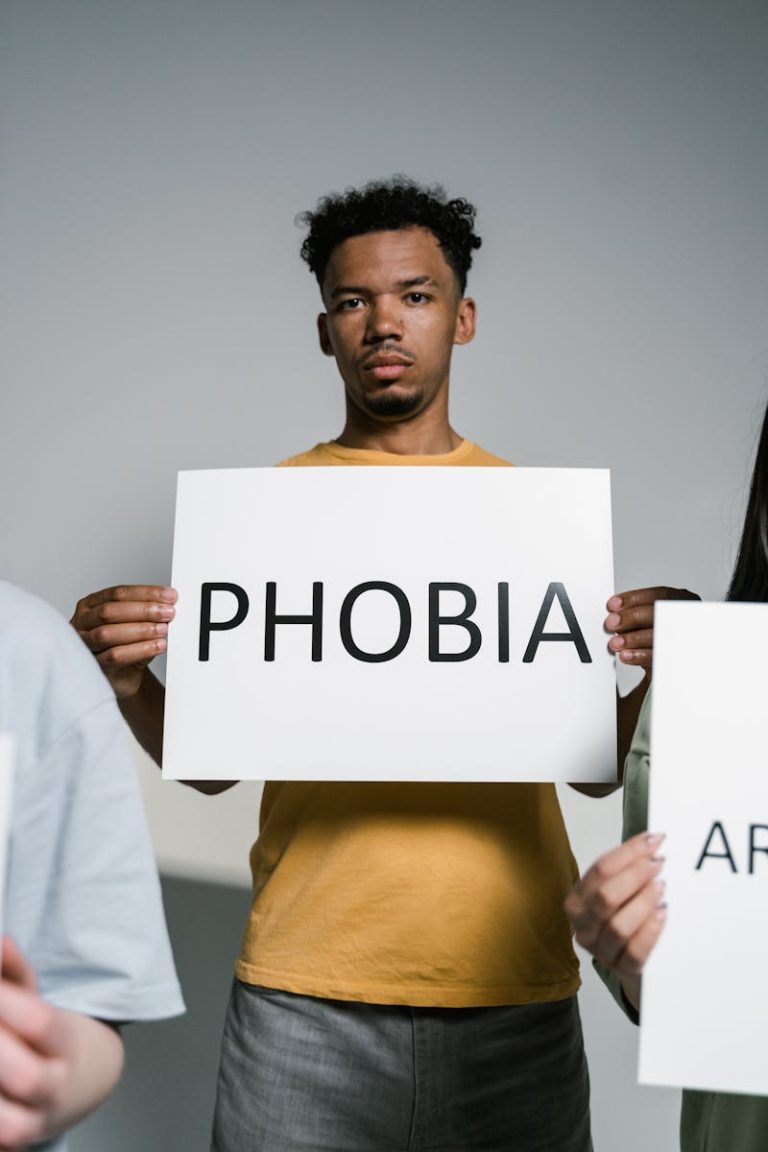 Man standing indoors holding a sign labeled 'Phobia', symbolizing fear or anxiety.