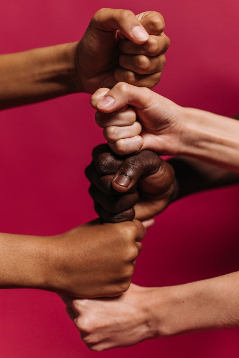 Close-up of diverse hands clenched together against a vibrant pink background symbolizing unity and strength.