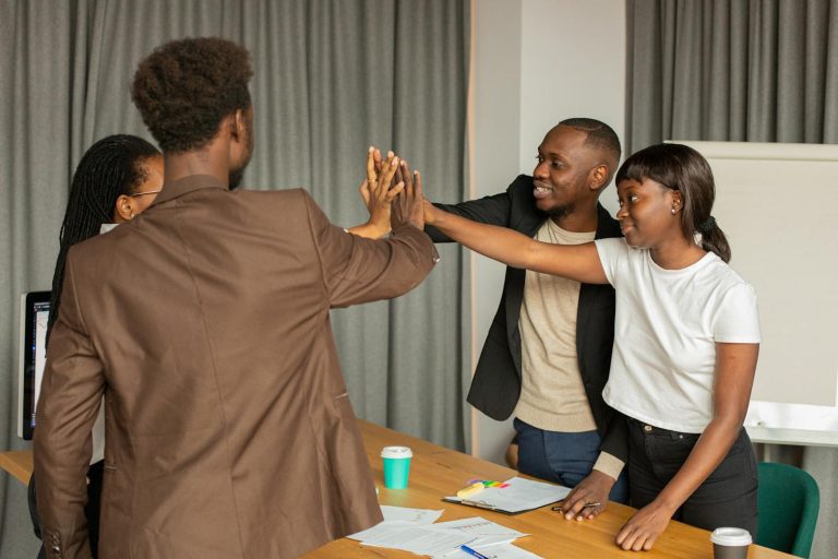 A group of diverse professionals high-fiving in an office setting, showcasing teamwork and collaboration.